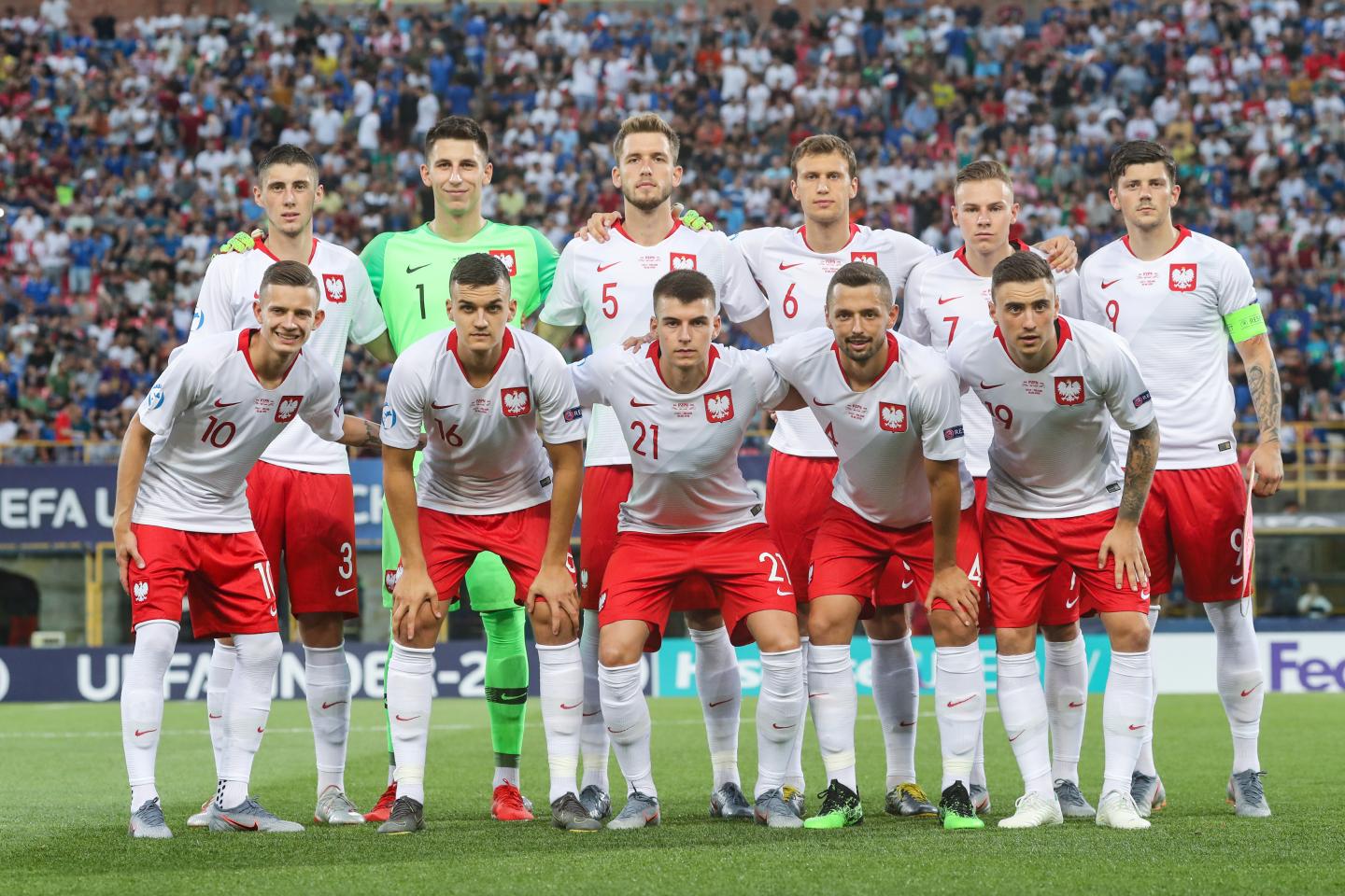 Reprezentacja Polski przed meczem z Włochami na młodzieżowych mistrzostwach Europy. Polacy w białych koszulkach z czerwonym kołnierzykiem oraz czerwonych spodenkach.