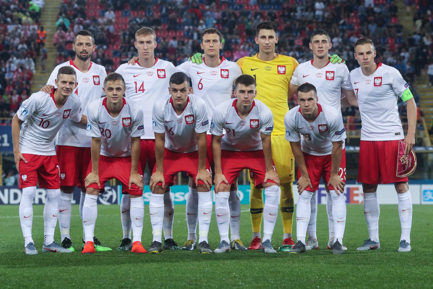 Grupowe zdjęcie reprezentacji Polski do lat 21 przed meczem z Hiszpanią, przegranym 0:5. Polacy w białych koszulkach i czerwonych spodenkach. Bramkarz Kamil Grabara na żółto.