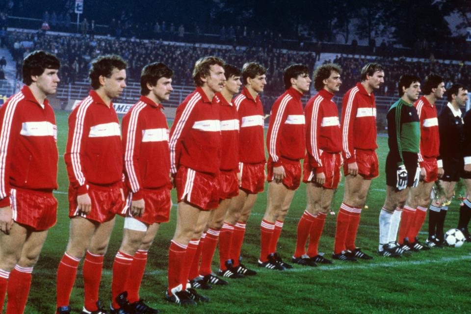 Reprezentacja Polski w czerwonych bluzach dresowych z białym poziomym pasem, czerwonych spodenkach i czerwonych getrach. Zdjęcie przed meczem z Grecją na stadionie Górnika Zabrze w 1984 roku.